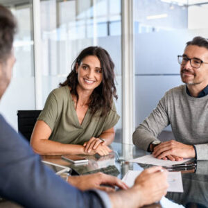 Smiling mature couple meeting with bank manager for investment. Beautiful mid adult woman with husband listening to businessman during meeting in conference room in modern office. Happy middle aged couple meeting loan advisor to buy a new home.